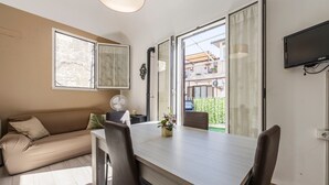 Een moderne woonkamer met een bank, eettafel, stoelen, een televisie en een glazen schuifdeur die uitkomt op een balkon.