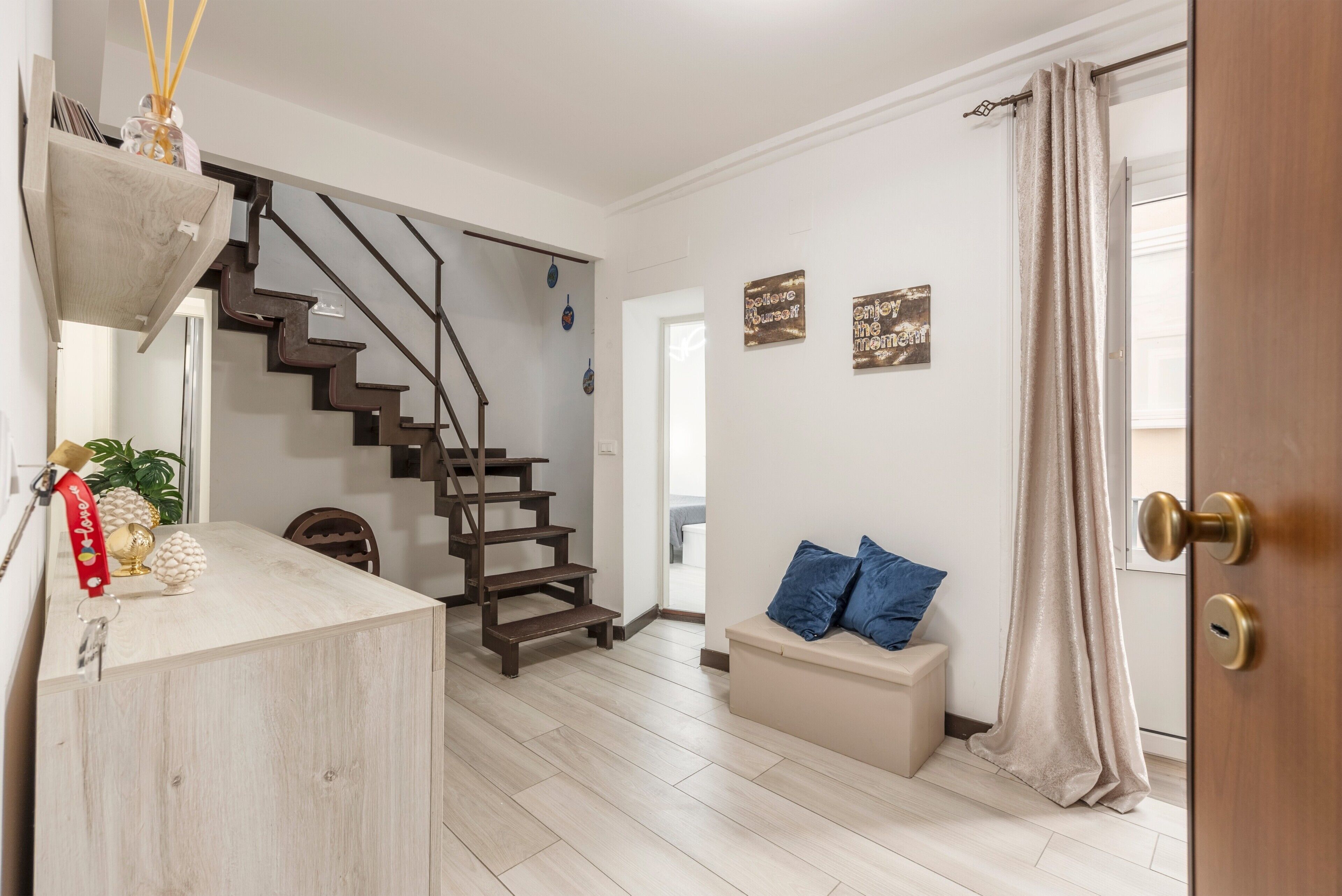 A staircase leading to a second floor, a wooden bench with blue cushions, and a door with a curtain.