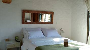 A bedroom with a wooden ceiling, a bed with white bedding, a green throw blanket, a bedside table with a lamp, and a mirror on the wall.