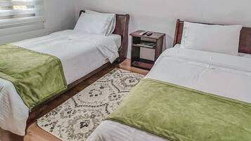 Una habitación con dos camas, cada una con una manta verde, una mesita de noche con un teléfono y una alfombra estampada.