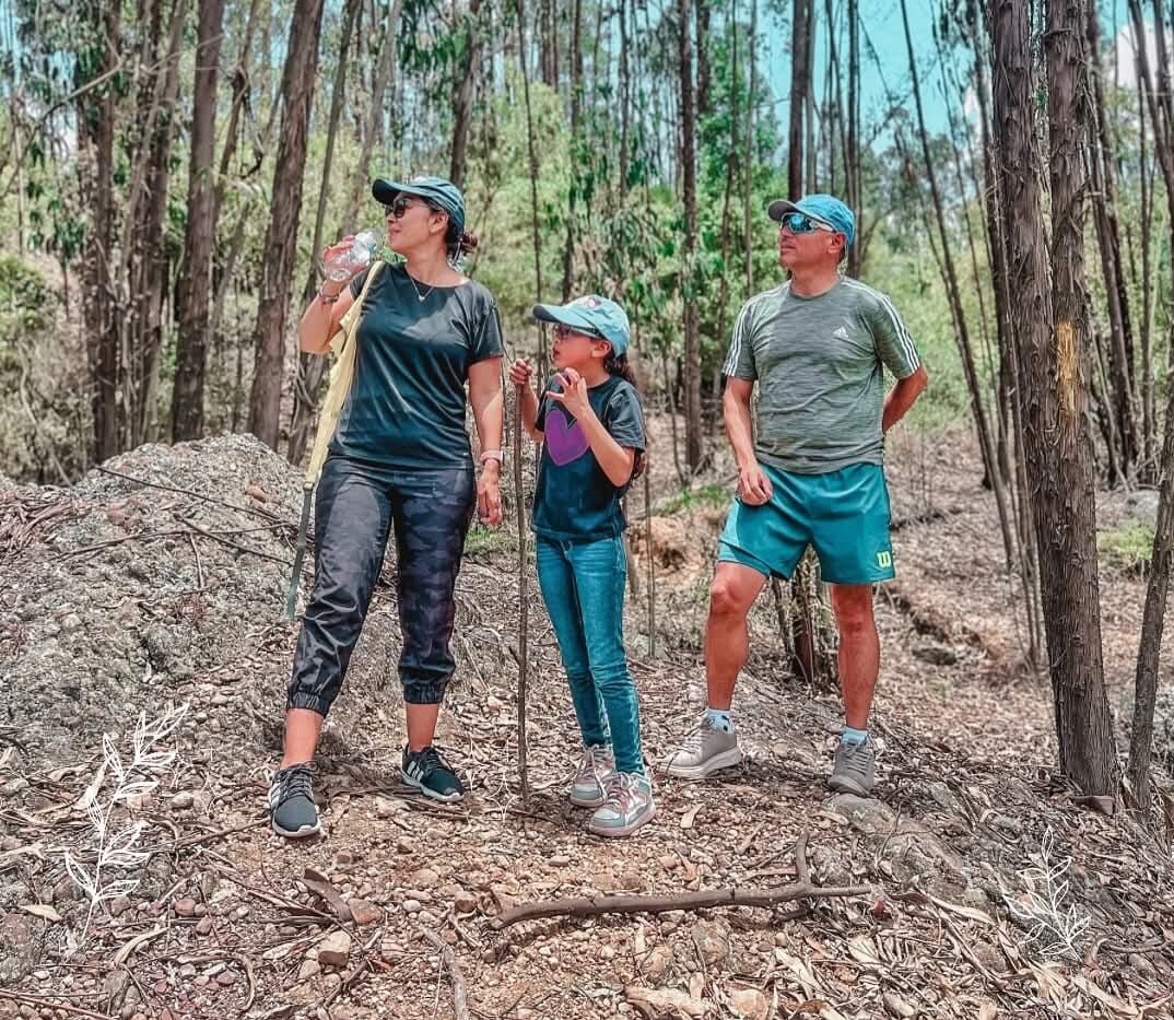Tres personas de pie en una zona boscosa con árboles y un montículo de rocas.