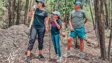 Tres personas de pie en una zona boscosa con árboles y un montículo de rocas.