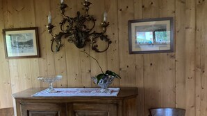 Una habitación con paneles de madera, un mueble de madera, dos cuadros enmarcados, una araña y una silla.