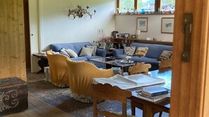 Una sala de estar acogedora con techo de madera, un conjunto de sofás, una mesa de comedor con libros y una araña.