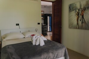 A bedroom with a bed, pillows, a blanket, a painting on the wall, and a door leading to a bathroom.