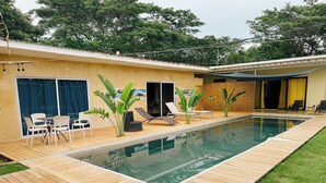 Une piscine avec une terrasse en bois, des chaises longues et une table avec des chaises.