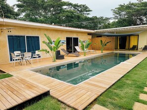 Une piscine avec une terrasse en bois, des chaises longues et une table avec des chaises.