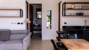 Un espace de vie moderne avec un canapé gris, une table à manger en bois et un coin cuisine doté d’étagères et d’un évier.