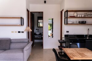 Un espace de vie moderne avec un canapé gris, une table à manger en bois et un coin cuisine doté d’étagères et d’un évier.