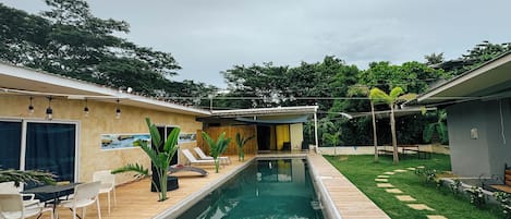A pool area with a wooden deck, lounge chairs, and a small table.