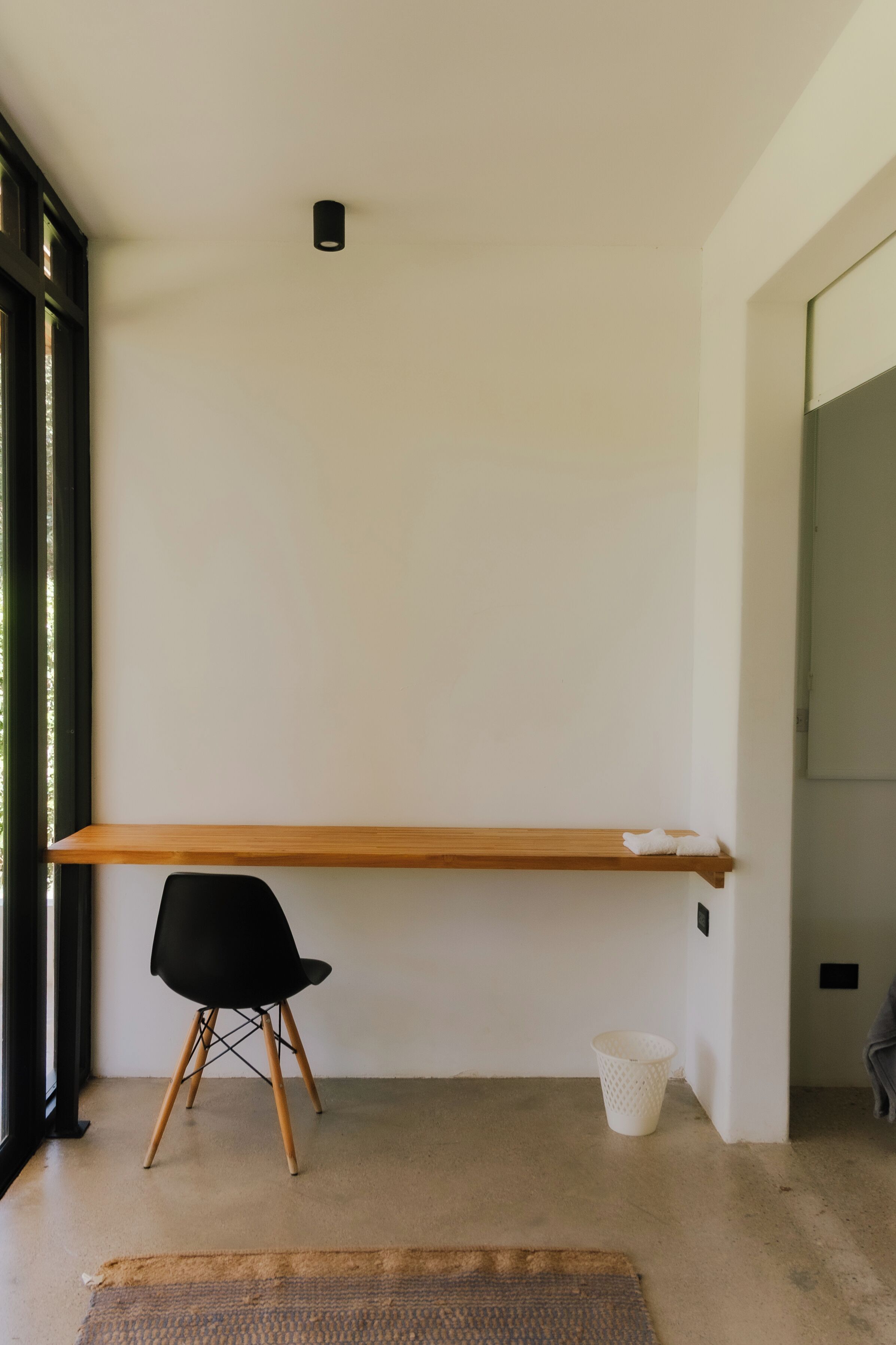 A minimalist room with a wooden desk, a black chair, and a small white basket.