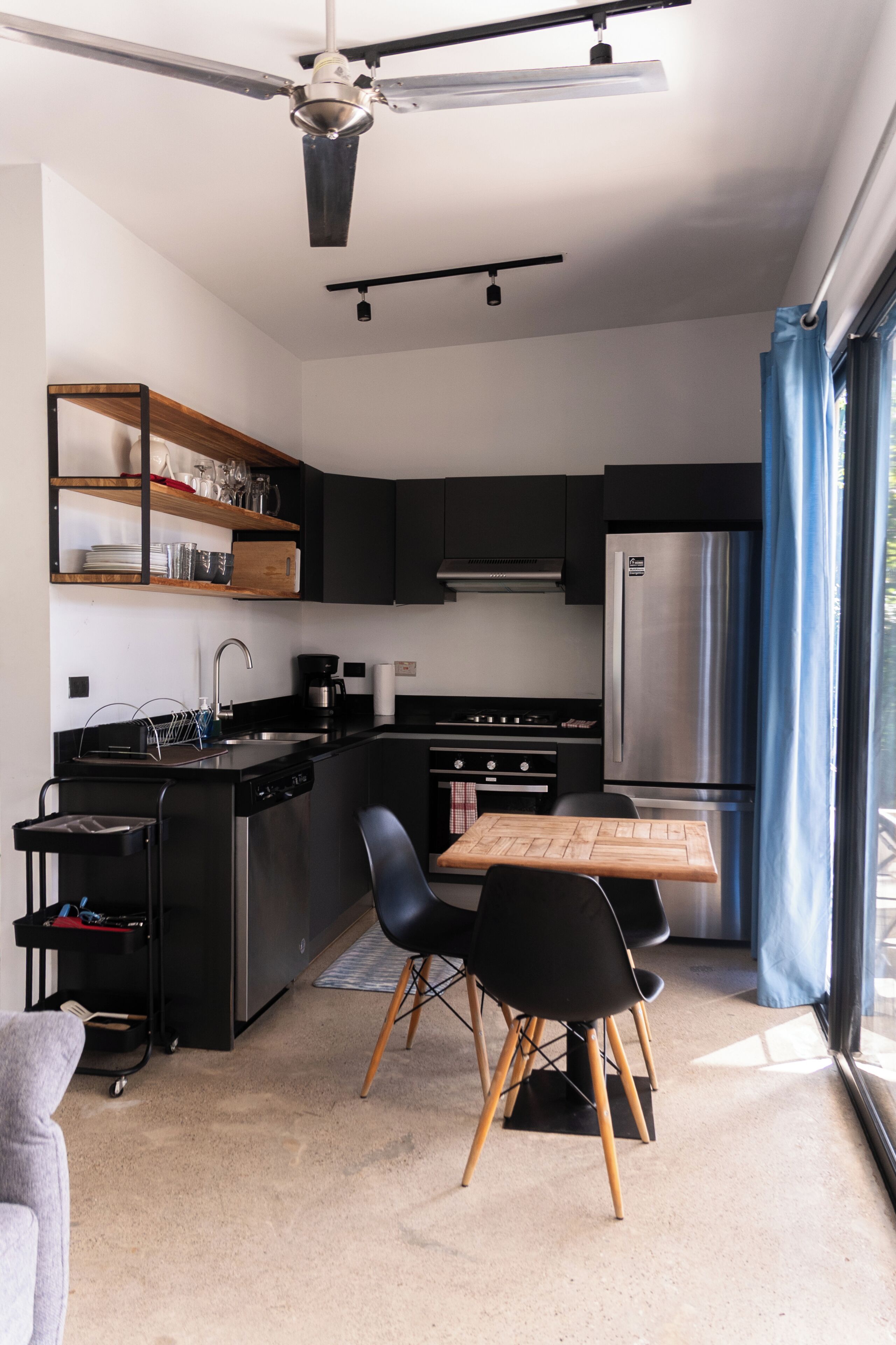 Een moderne keuken met een centraal eiland, zwarte keukenkastjes, roestvrijstalen apparatuur en een eetgedeelte met een houten tafel en zwarte stoelen.