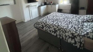Une chambre compacte comprenant un lit, une petite kitchenette et un téléviseur fixé au mur.