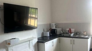Une cuisine avec des meubles blancs, un plan de travail noir, un four à micro-ondes, un grille-pain et un téléviseur à écran plat fixé au mur.