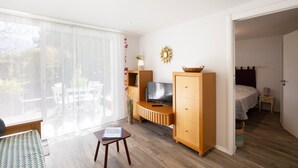 A modern living room with a TV, wooden cabinet, and a dining area with a bench. - Vacation Apartment by Lake Annecy in Sevrier (Sevrier)