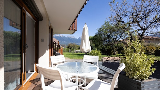 A patio with a round table and chairs, an umbrella, and a view of mountains. - Vacation Apartment by Lake Annecy in Sevrier (Sevrier)