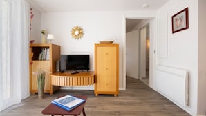 A living room with a TV, wooden cabinet, bookshelf, and a small table with a book. - Vacation Apartment by Lake Annecy in Sevrier (Sevrier)