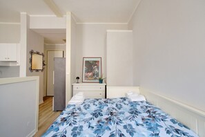 Un dormitorio con cama, cómoda, espejo, un cuadro enmarcado y una puerta que da a un pasillo.