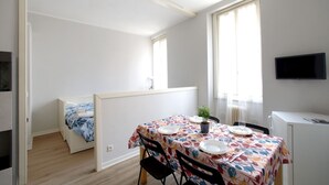 A small, well-lit room with a bed, a dining table set for two, a TV, and a window with curtains. - GuestHost - Cozy 50 sqm studio apartment, perfect for a stay of two people, located on the first floor of a building with elevator (NOT suitable for disabled people).The property is located in the San Zeno district, a few steps from the Museum and the ma (Verona)