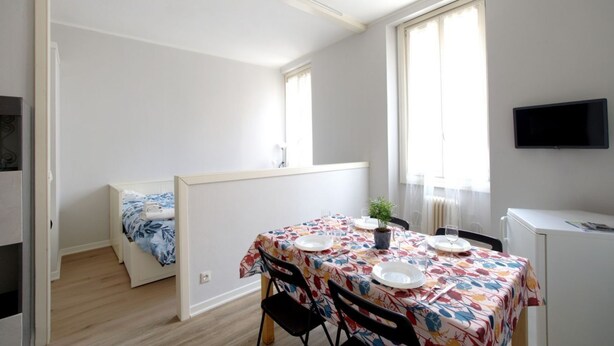 A small, well-lit room with a bed, a dining table set for two, a TV, and a window with curtains. - GuestHost - Cozy 50 sqm studio apartment, perfect for a stay of two people, located on the first floor of a building with elevator (NOT suitable for disabled people).The property is located in the San Zeno district, a few steps from the Museum and the ma (Verona)