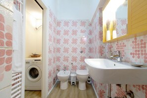Ein kleines Badezimmer mit Waschmaschine, zwei Toiletten, einem Waschbecken und einem Spiegel.