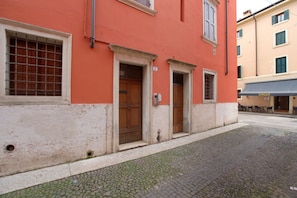 Ein Gebäude mit roter Fassade, eine gepflasterte Straße und eine sichtbare Tür mit der Hausnummer 7.