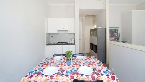 A compact kitchen with white cabinets, a dining table set for four with a colorful tablecloth, and a small potted plant. - GuestHost - Cozy 50 sqm studio apartment, perfect for a stay of two people, located on the first floor of a building with elevator (NOT suitable for disabled people).The property is located in the San Zeno district, a few steps from the Museum and the ma (Verona)
