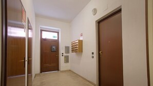 A hallway with wooden doors, a fire alarm, and a small shelf with items. - GuestHost - Cozy 50 sqm studio apartment, perfect for a stay of two people, located on the first floor of a building with elevator (NOT suitable for disabled people).The property is located in the San Zeno district, a few steps from the Museum and the ma (Verona)