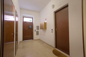 A hallway with wooden doors, a fire alarm, and a small shelf with items.