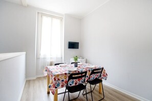 Ein Essbereich mit einem Tisch für zwei Personen, einem Topf mit Pflanze und einem an der Wand befestigten Flachbildfernseher.