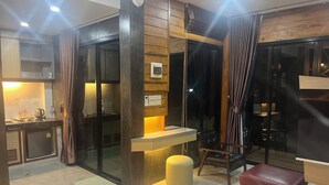 A modern hotel room with a kitchen area, a seating area with a table and chairs, and a large window with curtains. - Darisa home  ที่พักใกล้ตัวเมืองสุราษฎร์ธานี เพียง 6 กิโลเมตร บรรยากาศดีมาก (เมือง)