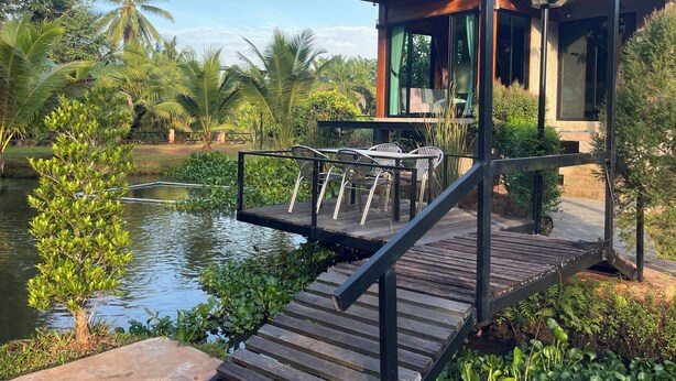 A modern building with a wooden deck and outdoor seating area overlooking a body of water. - Darisa home  ที่พักใกล้ตัวเมืองสุราษฎร์ธานี เพียง 6 กิโลเ  มตร บรรยากาศดีมาก (เมือง)
