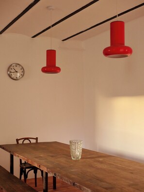 Un'area pranzo con tavolo in legno, sedie, un vaso di vetro e lampade a sospensione rosse.