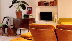 Een gezellige woonkamer met een houten plafond, een boekenplank, een televisie en een plant.