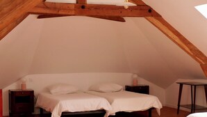 Een gezellig zolderkamertje met schuine wanden, houten balken en een enkel bed met witte beddengoed.