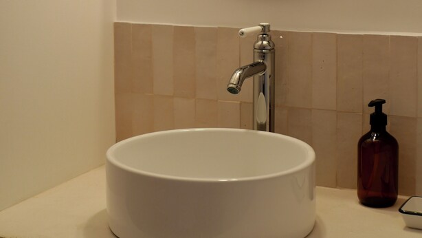 A bathroom with a round mirror, a white sink, a faucet, and a soap dispenser. - Ferme des Millonets - large gîte (Vienne-en-Arthies)