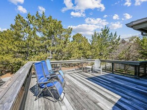 Una terraza de madera con sillas y una mesa azules y blancas, y una barandilla.