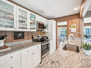 Cocina con encimeras de granito, muebles blancos y pileta de acero inoxidable.
