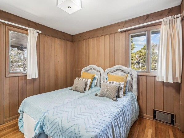 Un dormitorio con cama, paredes de madera y ventana con cortinas.