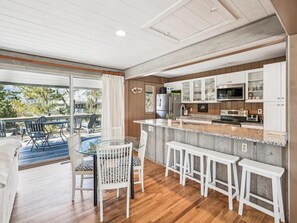 Una cocina moderna con una isla grande, taburetes de bar y un comedor con mesa y sillas de vidrio.