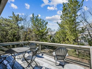 Una terraza de madera con mobiliario exterior, rodeada de árboles y un cielo despejado.
