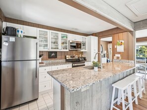 Una cocina moderna con una isla de granito, electrodomésticos de acero inoxidable y armarios blancos.