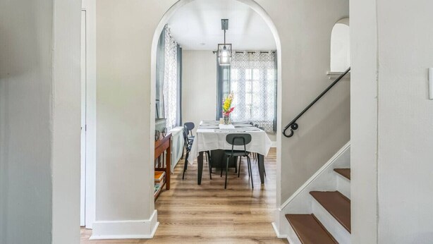 A hallway leading to a dining area with a table set for four, a staircase to the right, and a decorative light fixture above. - 4BR Pitt Suburbs Gem (Pittsburgh)