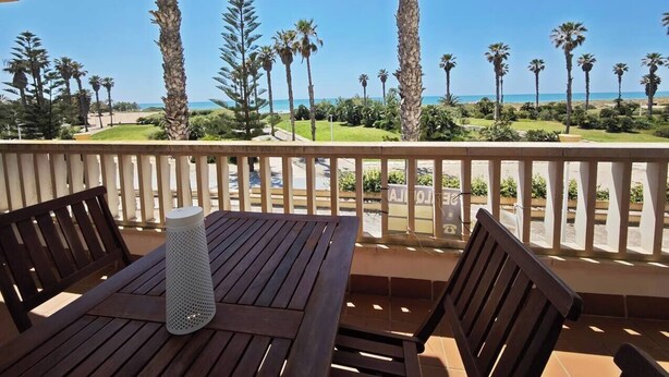A wooden table and chairs on a balcony with a view of palm trees and a beach. - Vista al Mar con terraza-Apartamento Costa Ballena (chipiona)