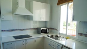 A compact kitchen with white cabinets, a microwave, a sink, and a window with a view of the outside. - Vista al Mar con terraza-Apartamento Costa Ballena (chipiona)