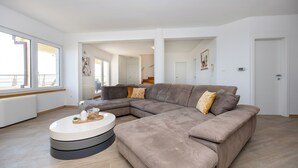 A modern living room with a large L-shaped sectional sofa, a round coffee table, and large windows providing natural light. - Breathtaking villa W Seaview & heated pool (Kučine)