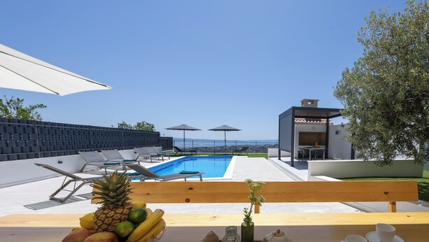 A poolside area with a wooden table, fruit bowl, and two white cups. - Breathtaking villa W Seaview & heated pool (Kučine)