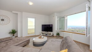 A modern living room with a sectional sofa, a coffee table, a flat-screen TV, and a large window offering a city view. - Breathtaking villa W Seaview & heated pool (Kučine)