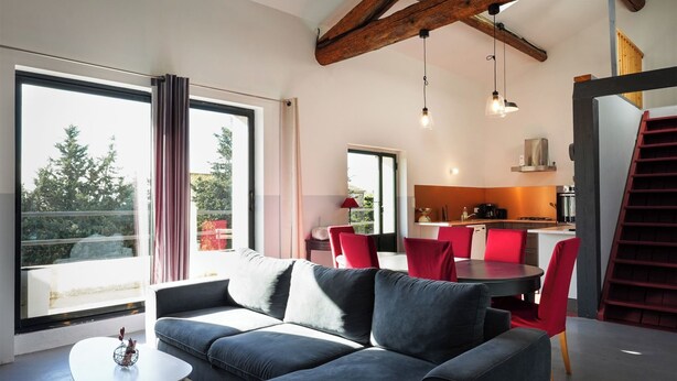 Un salón moderno con sofá, mesa de comedor y sillas. Se observa una zona de cocina al fondo con estufa y armarios.