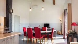 Un área de comedor con una mesa redonda y sillas rojas, un mueble de madera con cajones y un reloj en la pared.